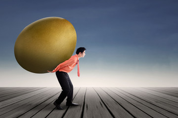 Young businessman is carrying a golden egg investment on his back