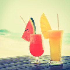 Colorful tropical fruit juice in the glasses on beach background - vintage tone
