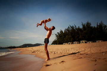father tosses up little daughter on sand beach