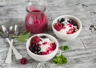 cottage cheese with berries and berry puree in a white bowl on a light wooden background, healthy Breakfast, snack