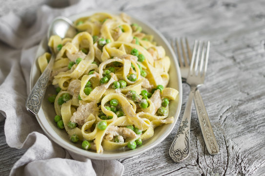 homemade pasta with chicken, green peas and cream sauce on an oval plate on a light wooden background