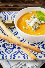 Cream of pumpkin soup with blue cheese and homemade grissini bread sticks in a white bowl