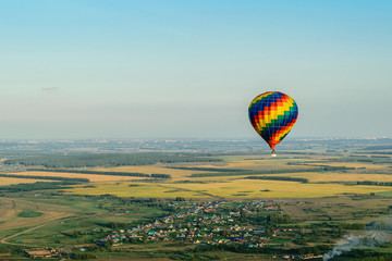 Colorful hot air balloon flying over the village, forest and fields