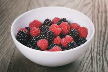 raspberries and blackberries in white bowl on wood table