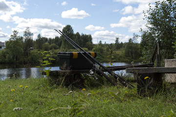Fototapeta premium Two rods and a lure box in front of a river on a grass covered place