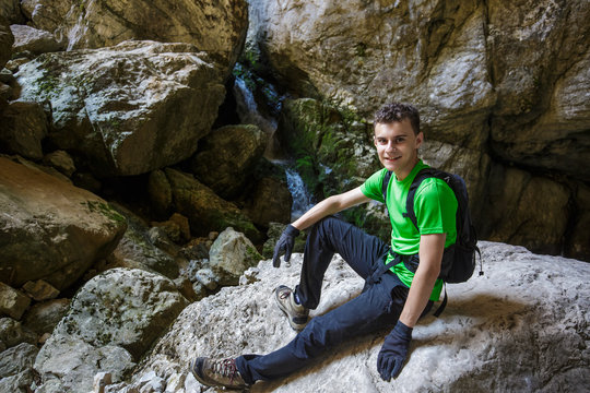 Happy teenager hiking near a waterfall in a cave