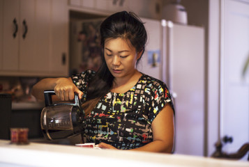 Cute Asian woman making coffee in kitchen, at home