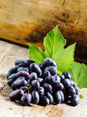 Blue grapes with leaves on old wooden background, selective focu