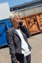 Geschäftsfrau steht bei Containern und telefoniert