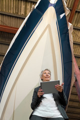 Frau mit Tablet vor einem Boot in einer Lagerhalle