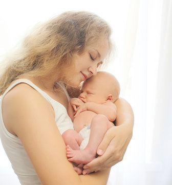 Young loving mother tenderly holds on hands sleeping infant at h
