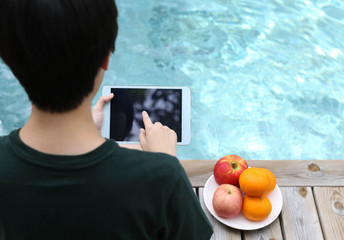 Young people sitting by the swimming pool and using tablet compu