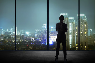 Woman standing in his office looking at the city at night