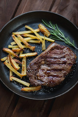 Close-up of grilled ribeye steak with potato in a frying pan