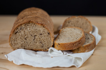 Pane fatto in casa ai sei cereali, tagliato a fette, su un tagliere di legno. Sfondo nero