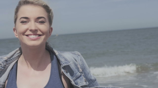Happy blonde woman in denim jacket sending a kiss on lonely beach. Happy young woman in denim jacket having fun time on lonely beach.
