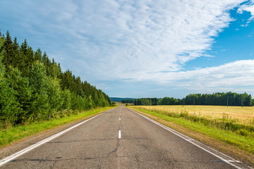 Highway in northen countryside with forest and wheat fields on a summer day