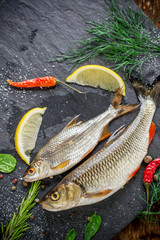 Fresh fish ide on a black stone slab surrounded by herbs, slices of lemon