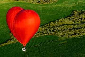 Red balloon in the form of heart over green fields and forests