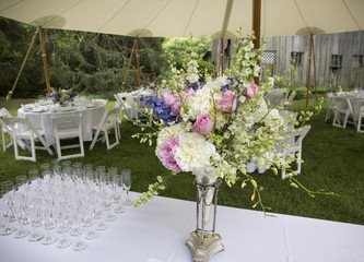 Flower arrangement and glasses and tables set up for outdoor wedding.