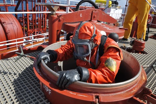 man in chemical suit entering inside cargo tank on deck of chemical tanker for cleaning operation