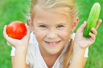 Happy little girl sitting on the grass with a vegetables at the