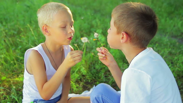 Two boys dressed in white, blowing dandelions on each other