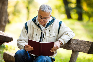 Happy senior man reading book in park in autumn day