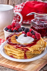 Pancakes with cream, raspberries and blackberries on the table