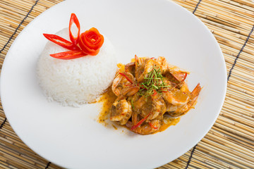 Curry fried shrimps and cooked rice in white dish closeup on table with wooden background