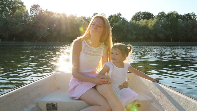 Young attractive mom and her daughter ride on the boat and doing a selfie.
