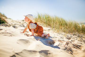 Fototapeta na wymiar Cute toddler climing up on a sandy hill on the beach