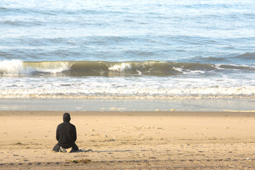 A lone man on sandy beach watching the ocean waves