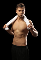 Fototapeta na wymiar Muscle young man holding towel on dark background