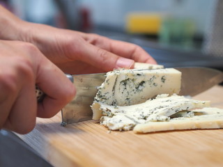 Hands slicing blue cheese with a knife
