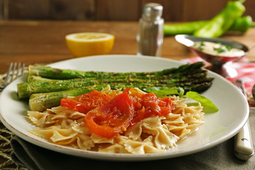 Roasted asparagus and tasty pasta with vegetables on plate on wooden table background