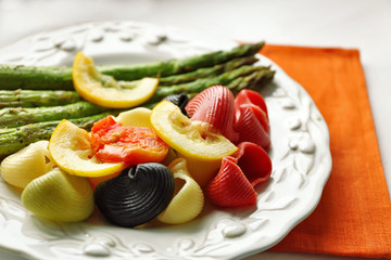 Roasted asparagus and tasty colorful pasta with vegetables on plate on wooden table background