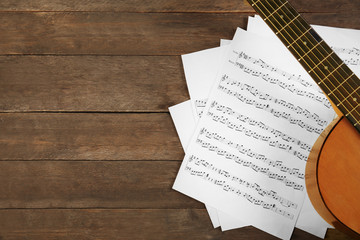 Music recording scene with guitar and music sheets on wooden table, closeup