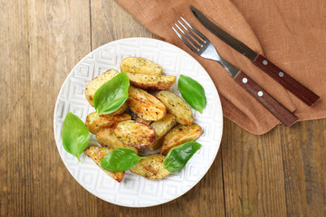 Baked potatoes with basil leaves in white plate on wooden table, top view