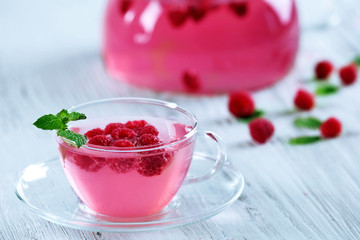 Cup and teapot of raspberry drink with berries on wooden table close up