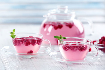 Cups and teapot of raspberry drink with berries on wooden table close up