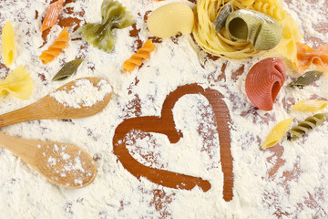 Row pasta with wooden spoons on flour background