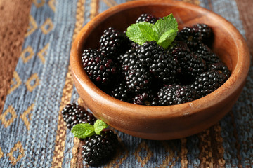 Ripe blackberry in bowl on color wooden background