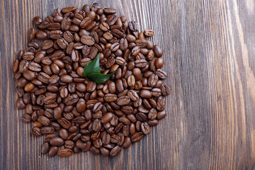 Coffee beans with leaves on wooden table close up
