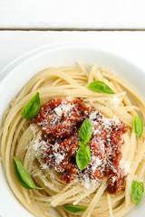 Spaghetti Bolognese with parmesan cheese in white bowl, on color wooden background
