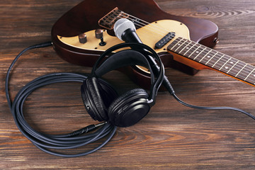 Electric guitar with microphone and headphones on wooden table close up