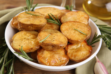 Delicious baked potato with rosemary in bowl on table close up