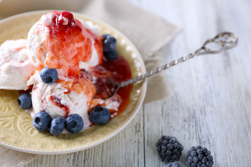 Delicious ice cream with fresh frozen berries and sauce, on color wooden background