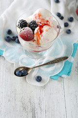 Delicious ice cream with fresh frozen berries and sauce, on color wooden background