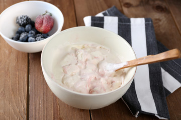 Delicious vanilla ice cream in bowl and frozen berries, on wooden background
